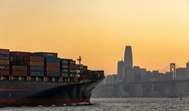 Cargo ship sails into the Port of Oakland at sunset.